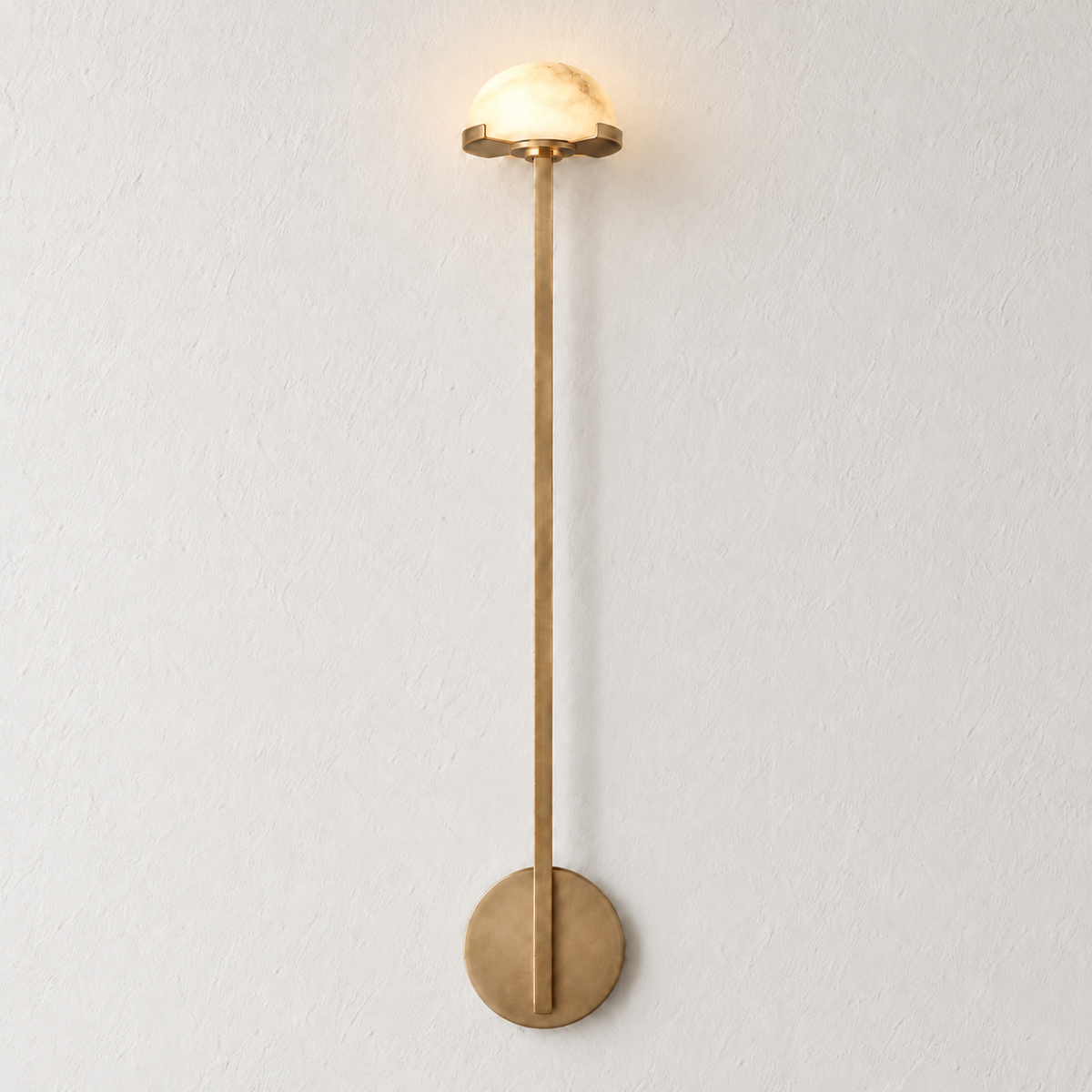 Tall brass wall sconce with a small alabaster dome, illuminated on ivory plaster.