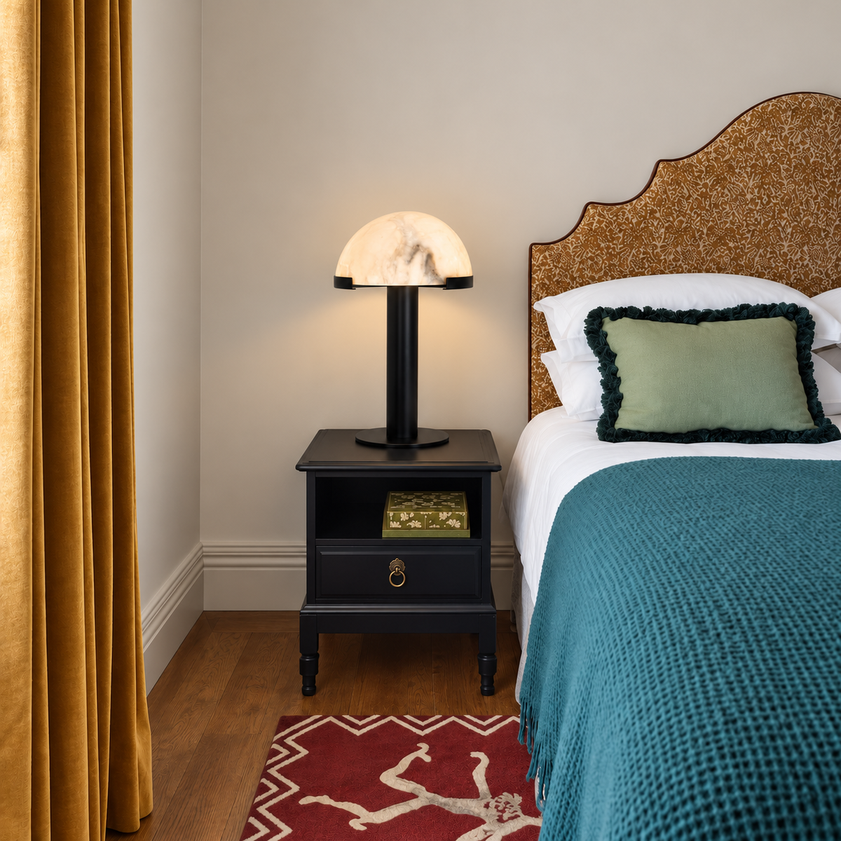 Black alabaster dome lamp on a bedside chest beside teal bedding.