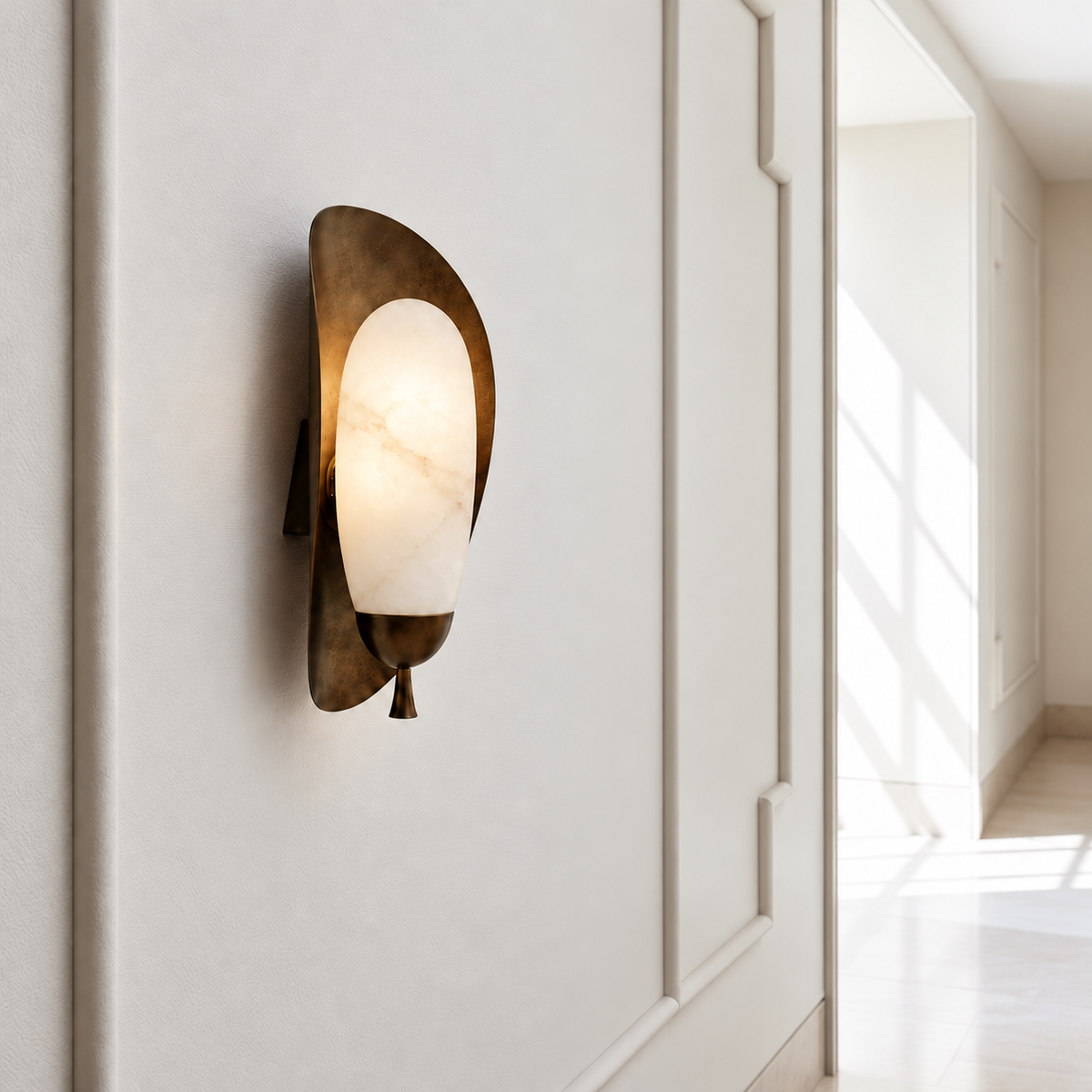 Alabaster wall sconce with a rounded shade and aged brass backplate in a bright paneled corridor.