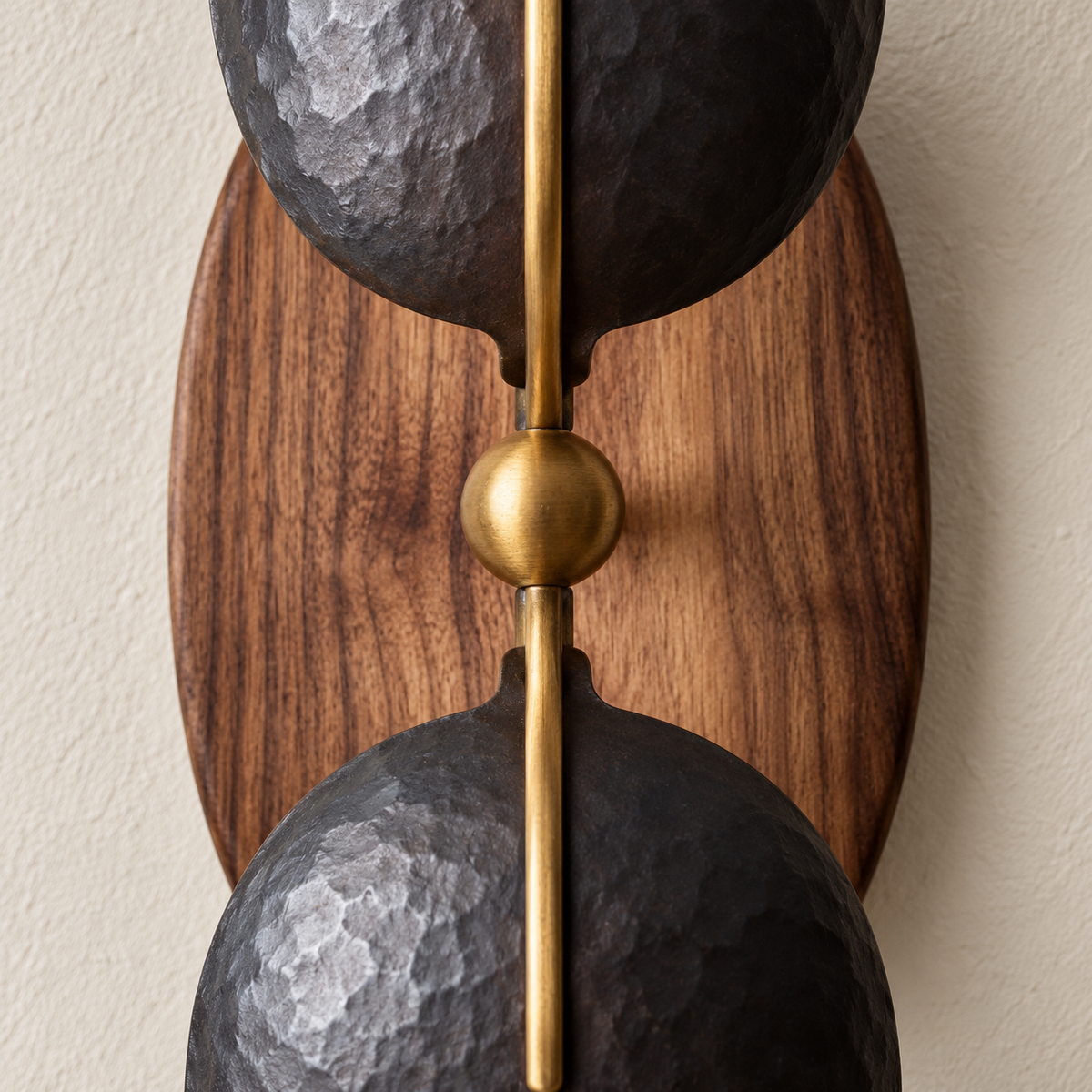 Close-up of hammered black iron, the brass centre fitting and walnut grain on the wall sconce.