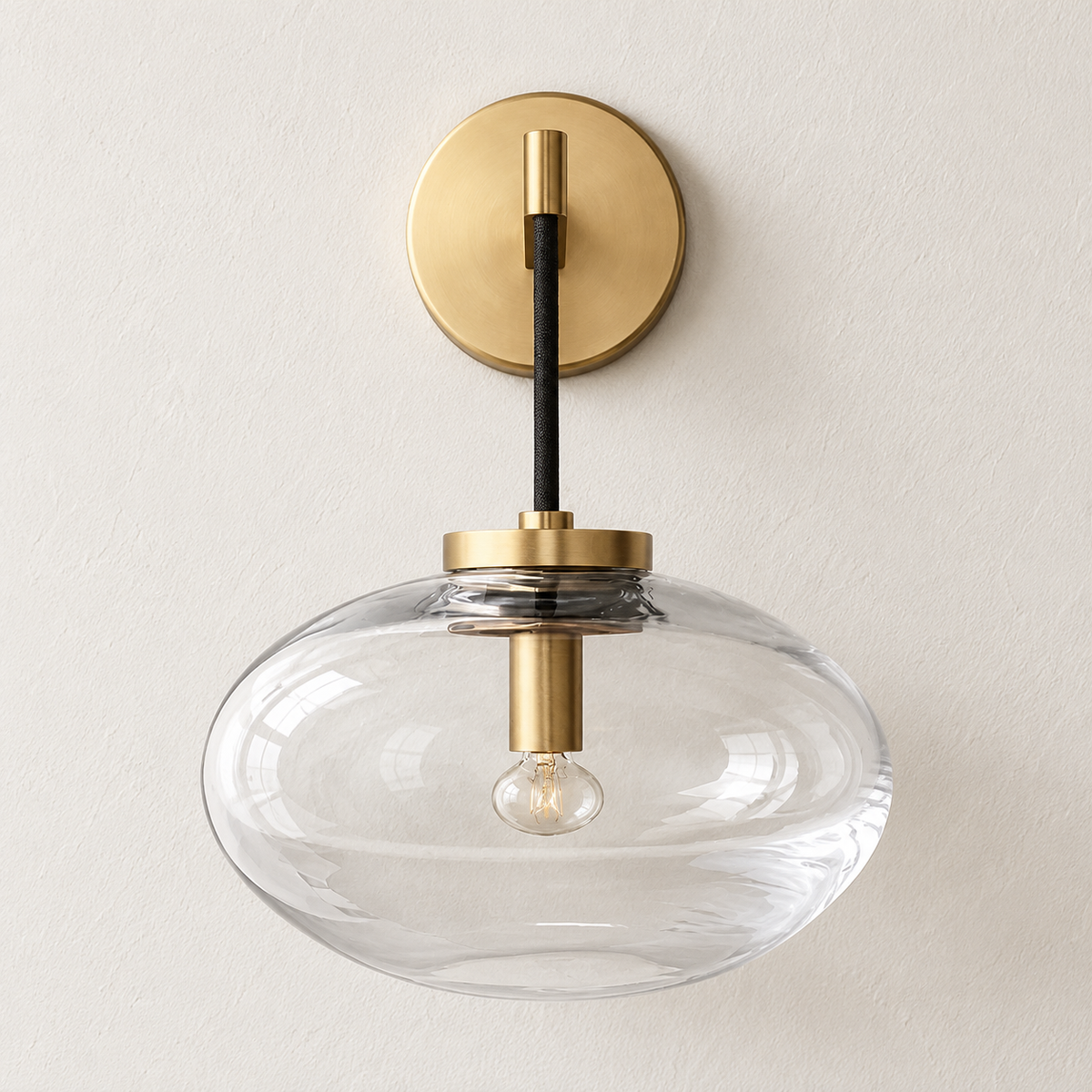 Brass wall sconce with a clear flattened glass shade, switched off on ivory plaster.