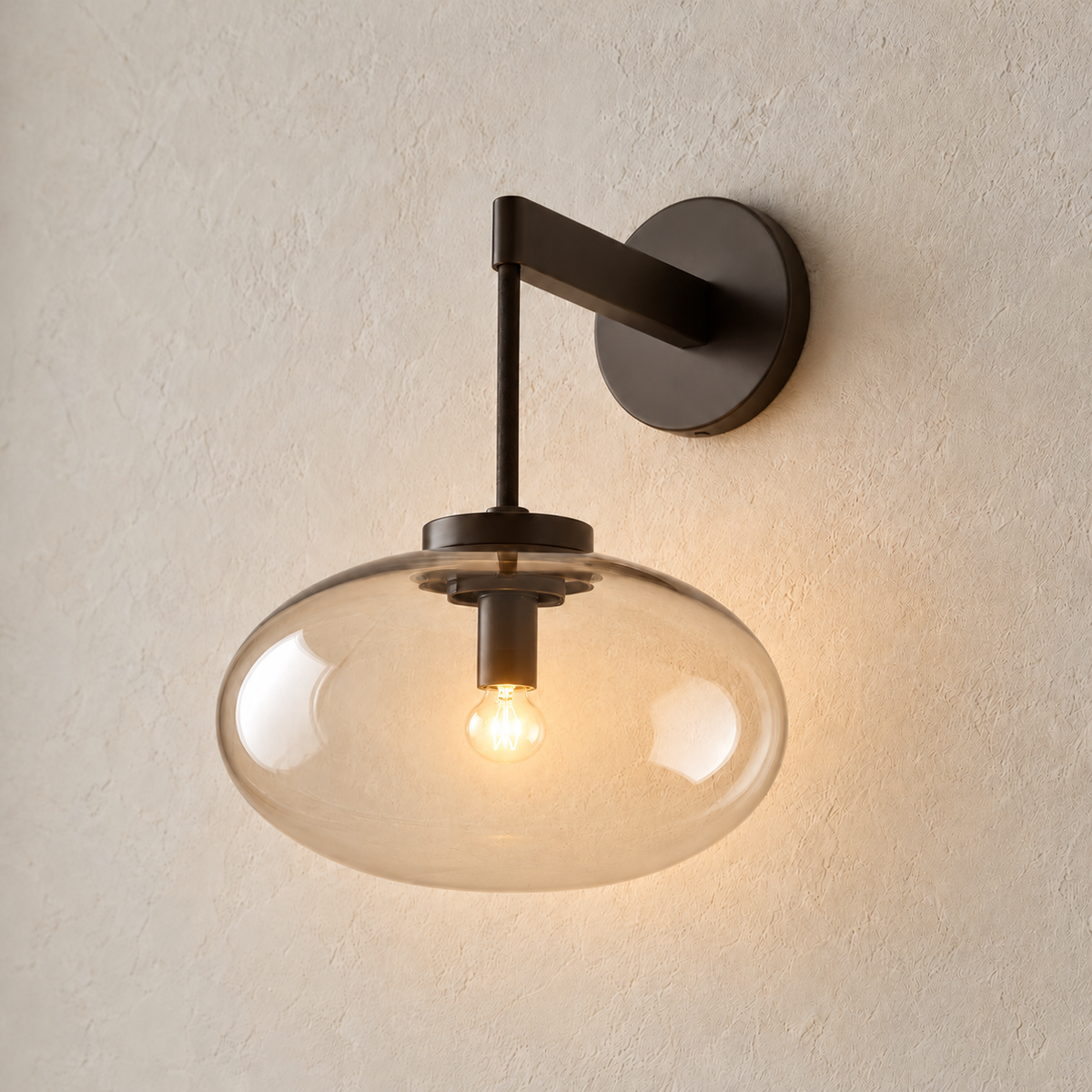 Black wall sconce with a lightly smoky glass shade, illuminated on ivory plaster.