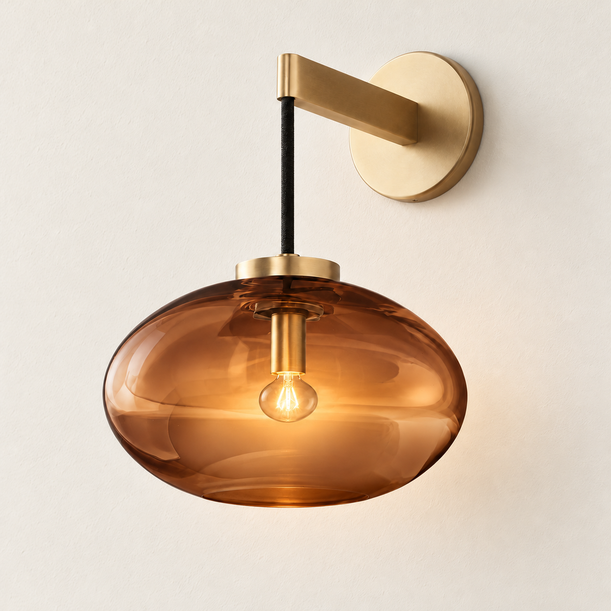 Amber glass wall sconce illuminated, with brass mounting hardware and a visible warm bulb.