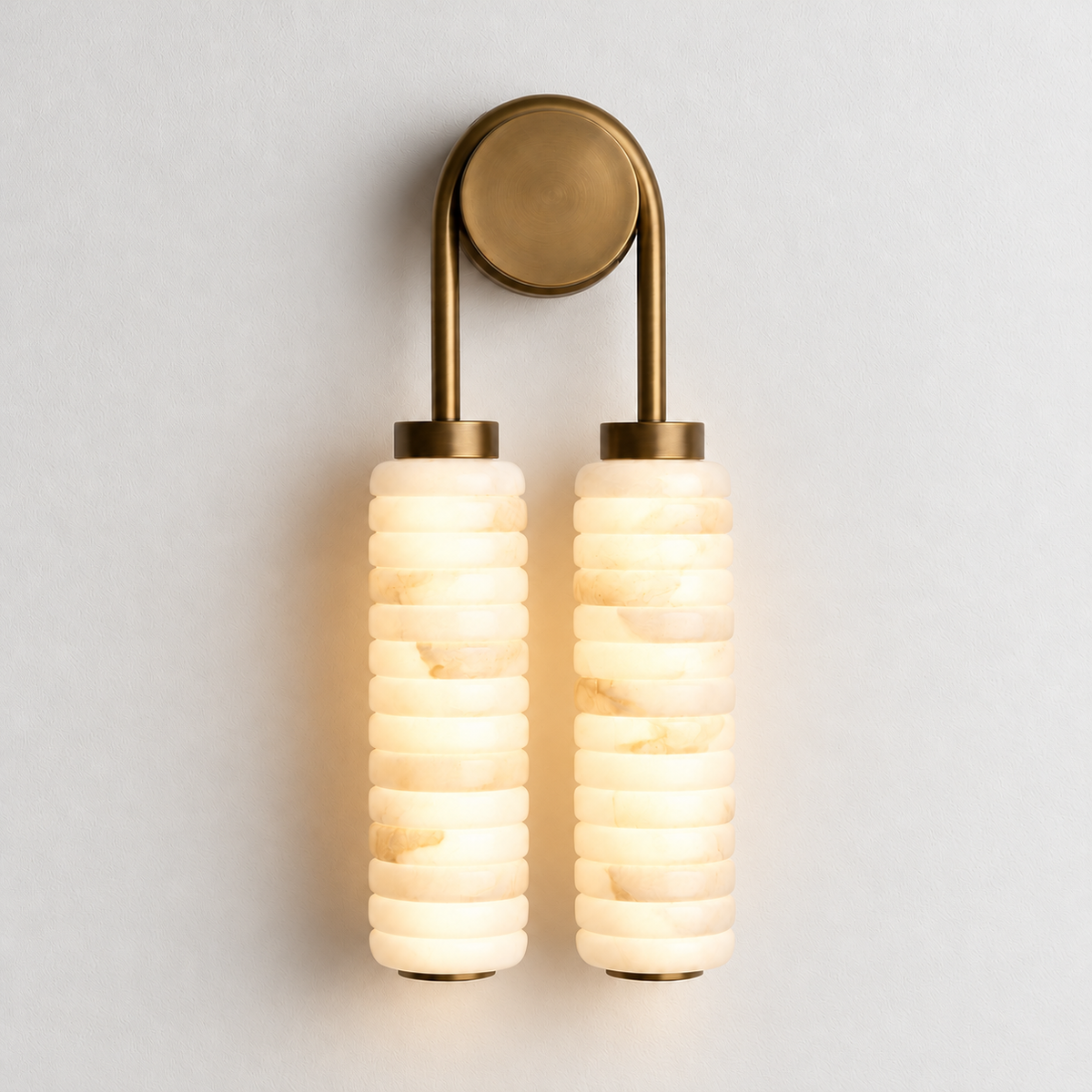 Double marble brass wall sconce illuminated on warm ivory.