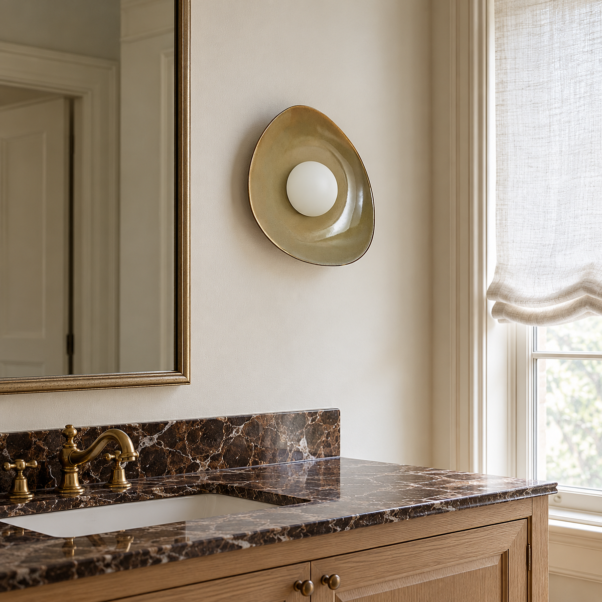 Olive ceramic globe sconce beside a bathroom mirror above a wooden vanity.