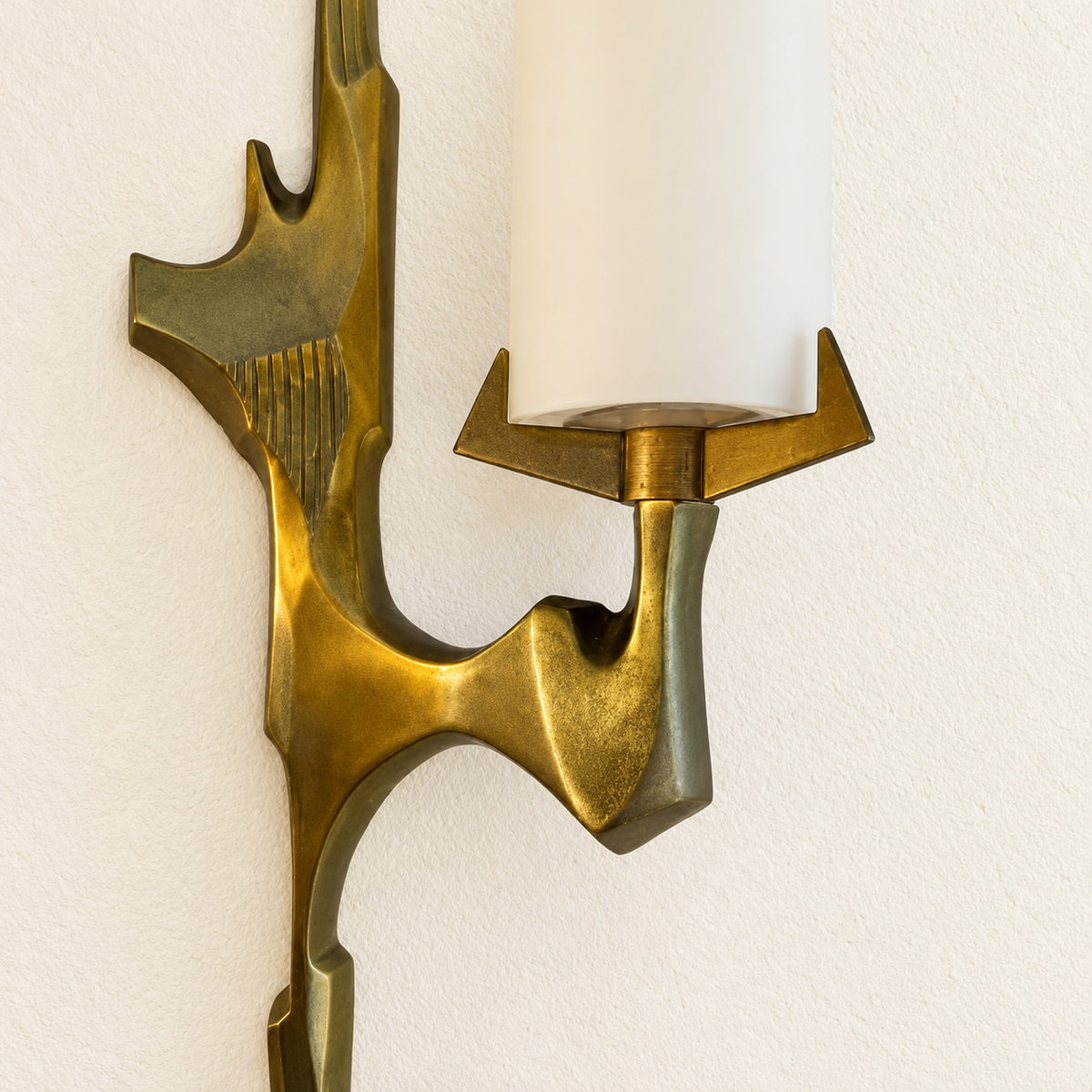 Close detail of sculptural brass sconce with two staggered opal glass shades and its material texture.