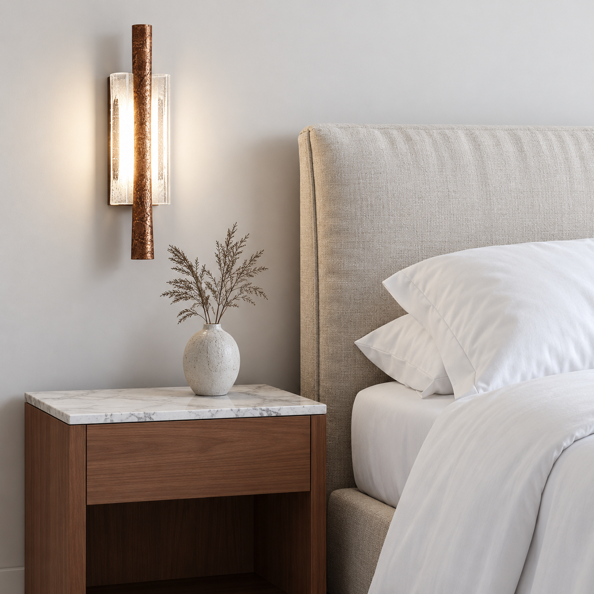 Textured brass wall sconce with clear curved glass mounted above a bedside table in natural daylight.