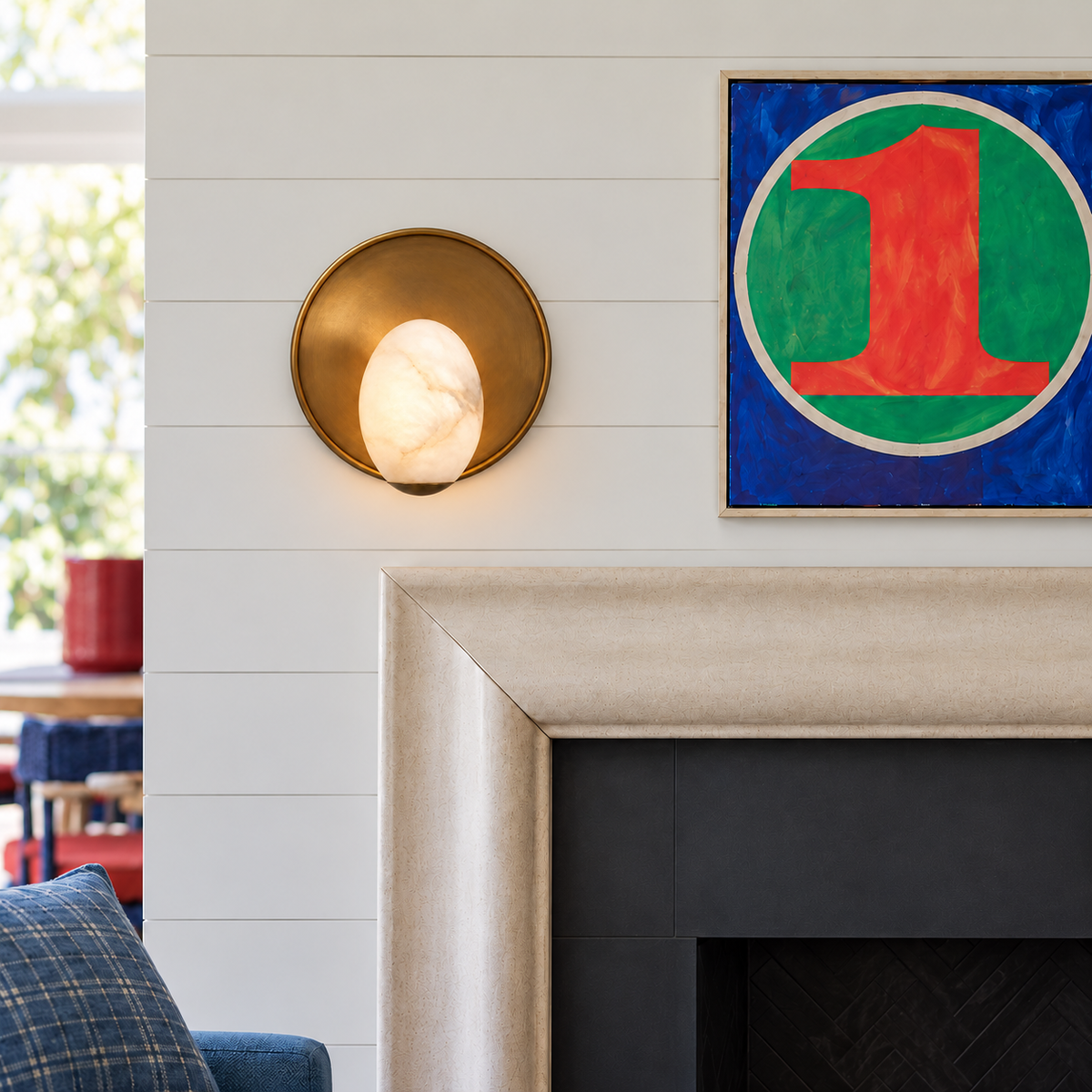 Round brass and alabaster wall sconce above a fireplace mantel beside blue living-room seating.