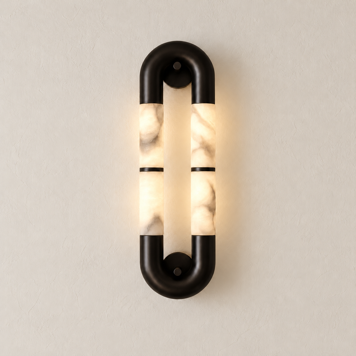 Elongated alabaster oval wall sconce with black metal connectors illuminated against the same warm ivory backdrop.