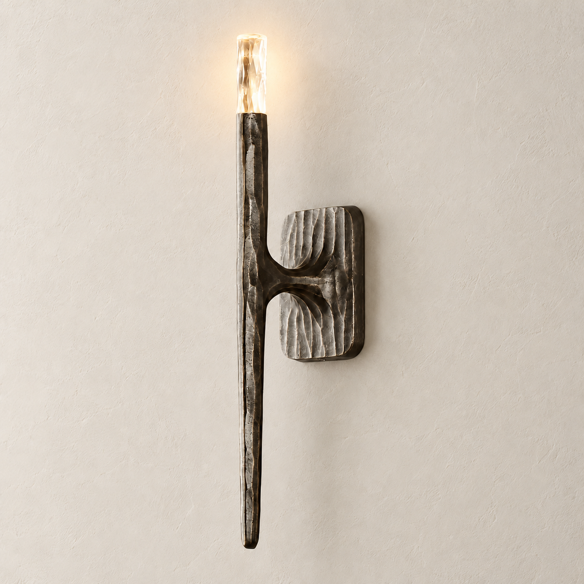 Sculptural stainless steel stick wall sconce illuminated on the same beige wall.
