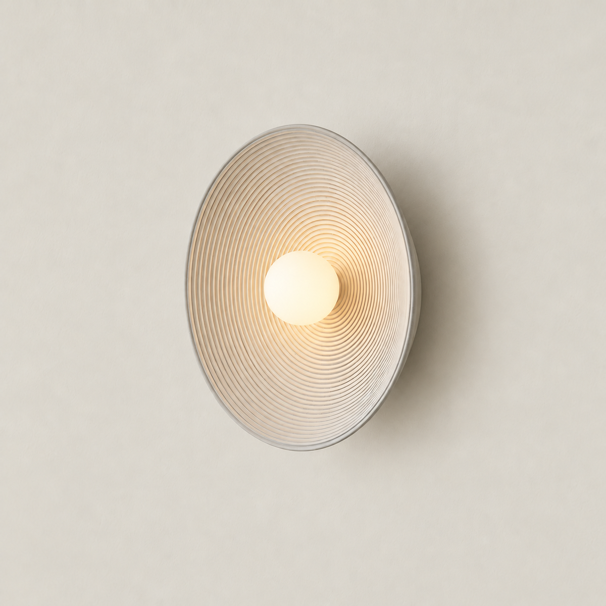 Illuminated cream ceramic disc wall lamp with concentric ridges and a central frosted glass globe.