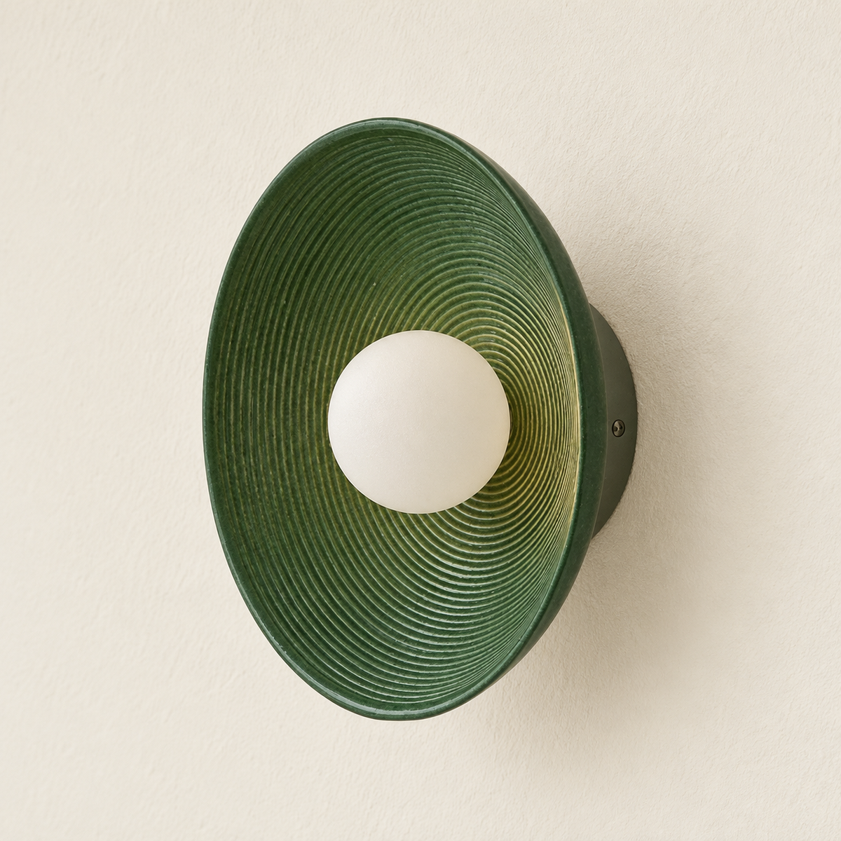 Angled view of the green ceramic disc wall lamp, showing its ridged face and shallow profile.