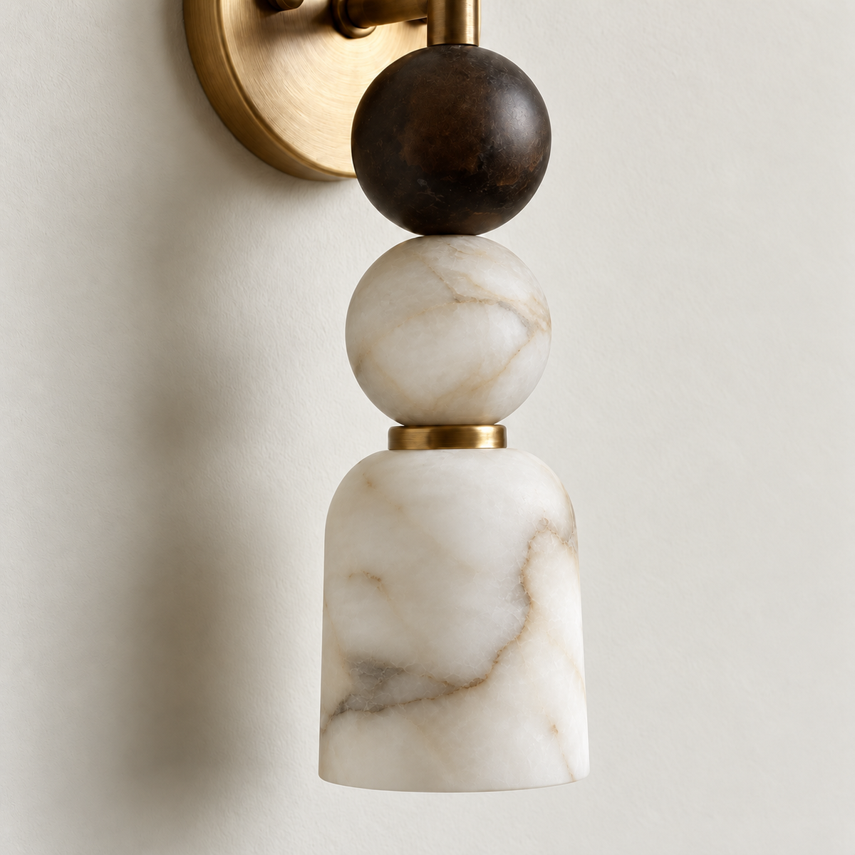 Close-up of the alabaster shade, pale stone sphere and brass collar on the wall sconce.