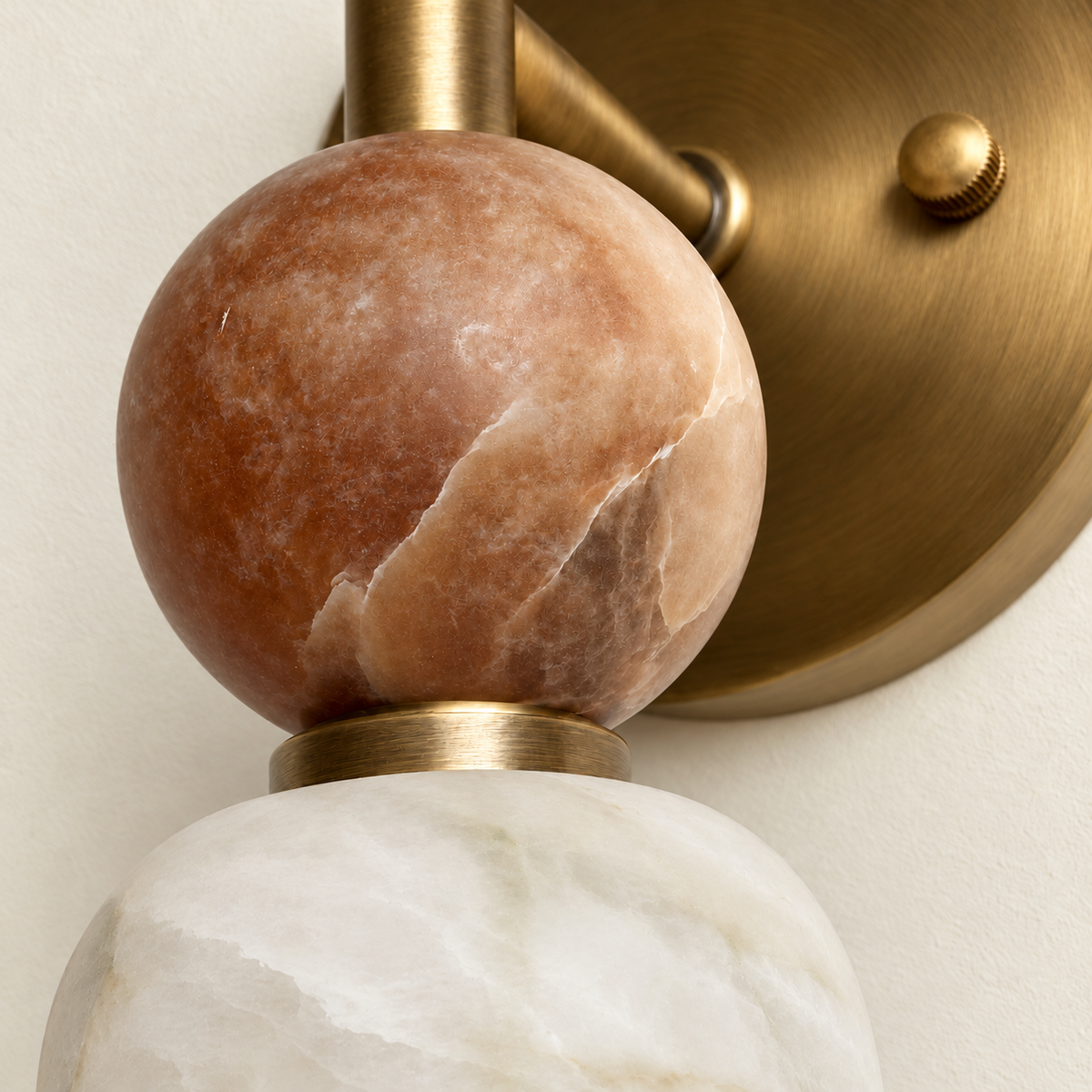 Close-up of the Totem Petite sconce’s Rosso marble sphere, brushed brass collar and natural alabaster veining.
