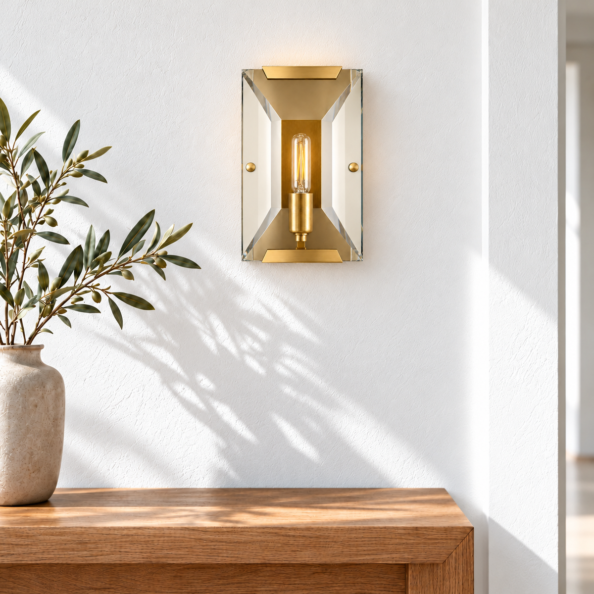 Brass and crystal wall sconce mounted above an oak entryway console in natural daylight.