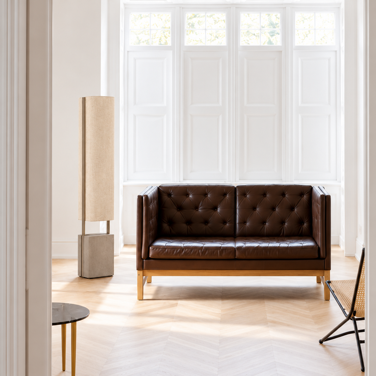 CLUJH025S floor lamp standing beside a dark leather bench in a bright room with white shutters and parquet flooring.