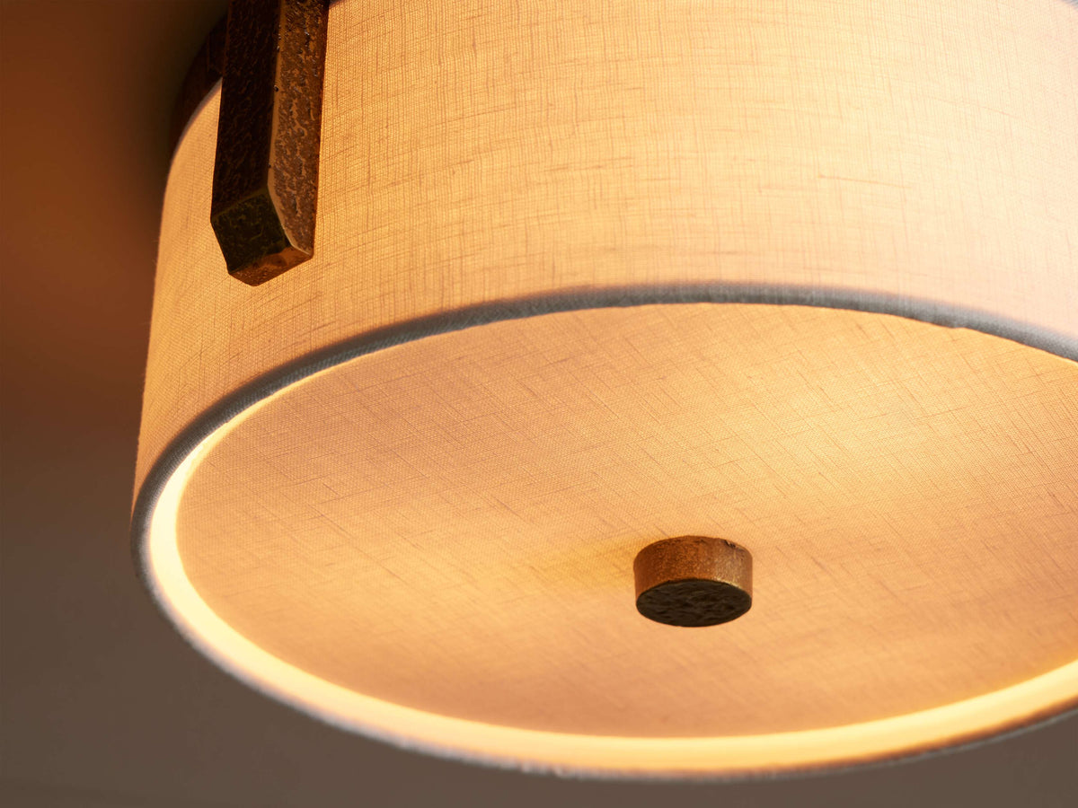 Detail of the Linnea flush mount showing a brass bracket, the linen shade and the brass center finial