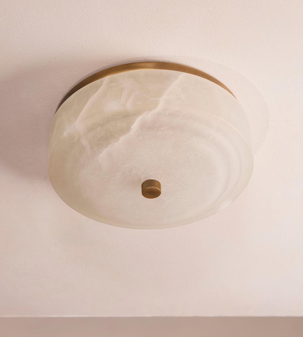 White alabaster flush mount, unlit, pale stone with faint veining and a knurled brass center knob