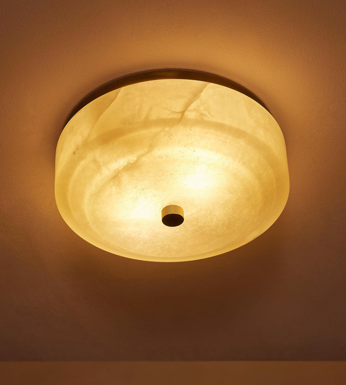 White alabaster flush mount lit at 2700K warm white on a dark ceiling