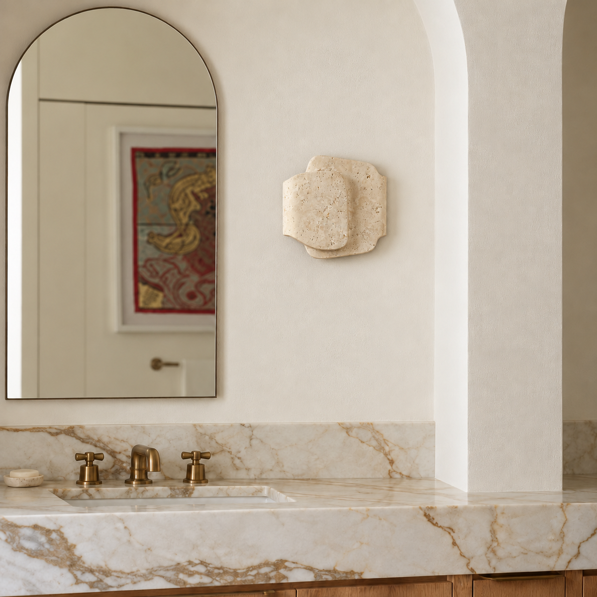 Layered travertine sconce beside an arched mirror above a marble bathroom counter.