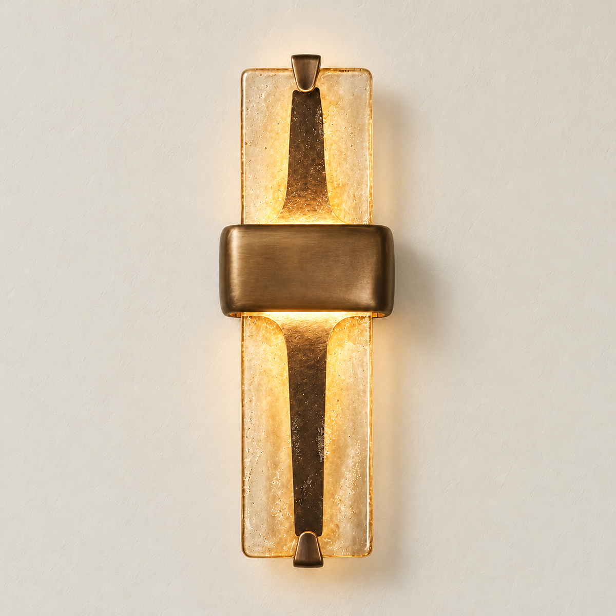 Textured glass and brass wall sconce illuminated with warm light against an ivory wall.