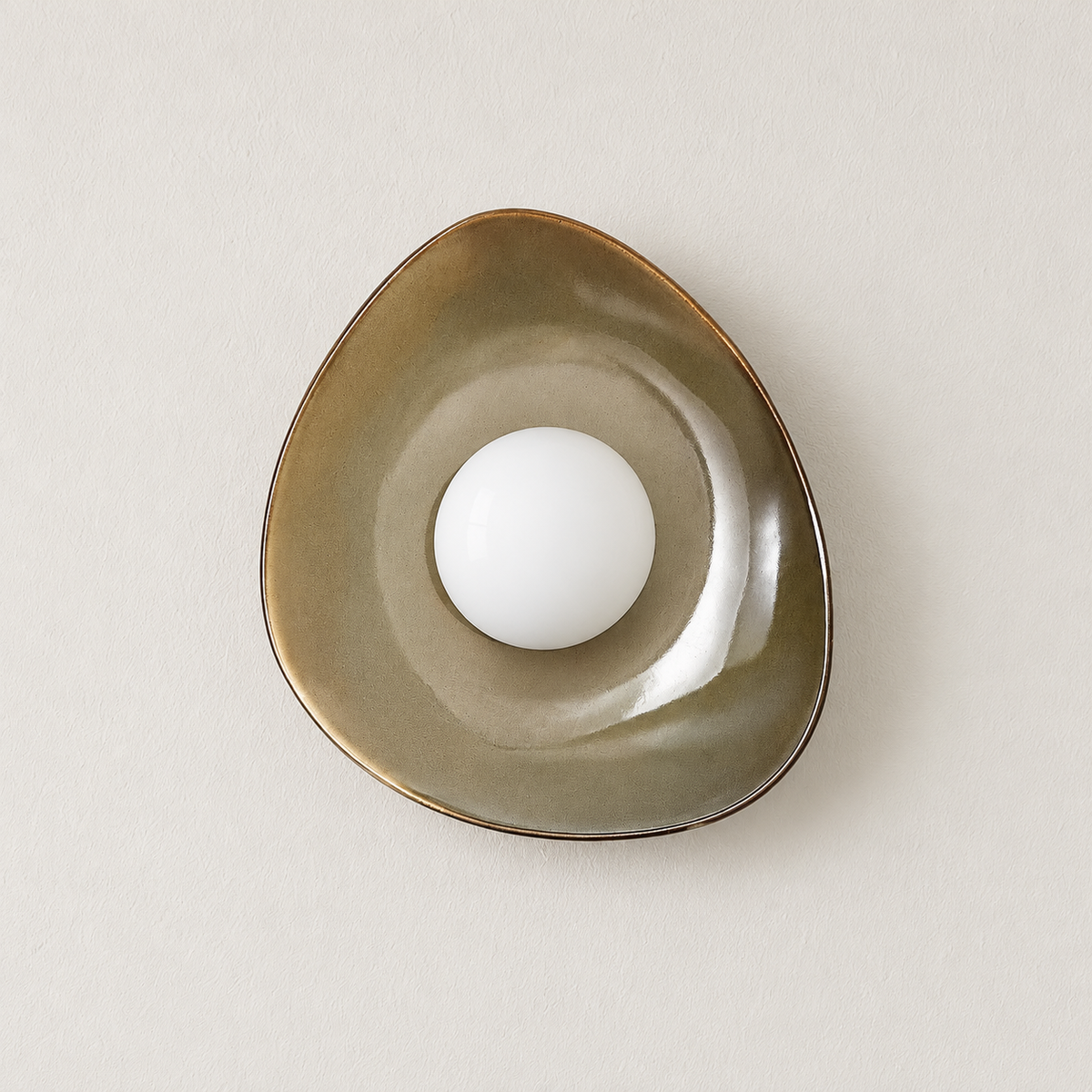 Olive ceramic wall sconce with an opal glass globe, switched off on ivory plaster.
