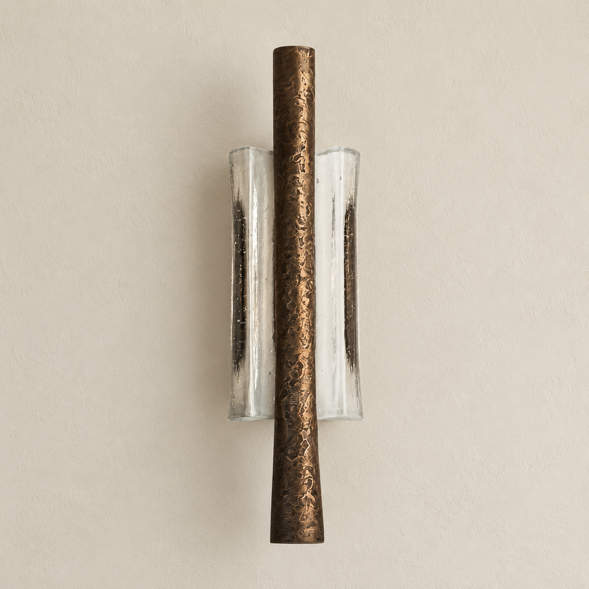 Textured brass wall sconce with clear curved glass unlit on warm ivory plaster.