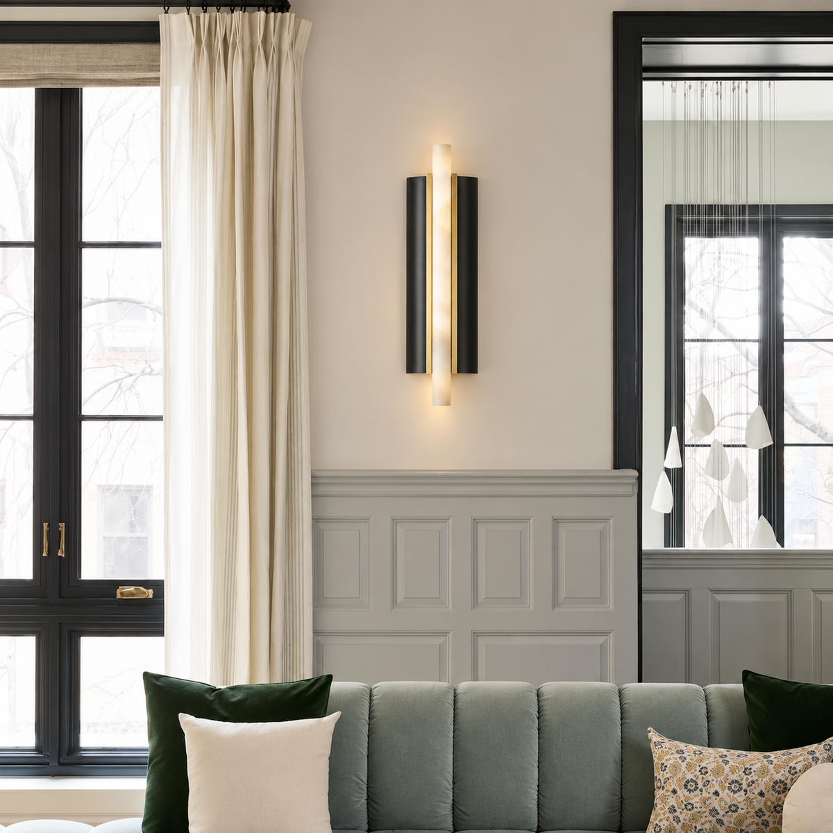 Alabaster tube sconce installed above a sofa beside a tall mirror.