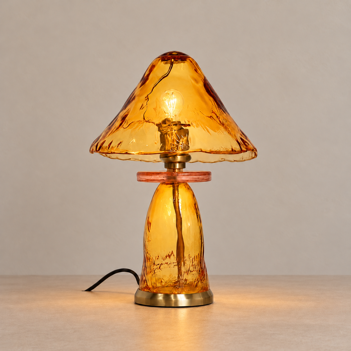 Amber glass table lamp with a pink glass collar and brass fittings, illuminated on a beige background