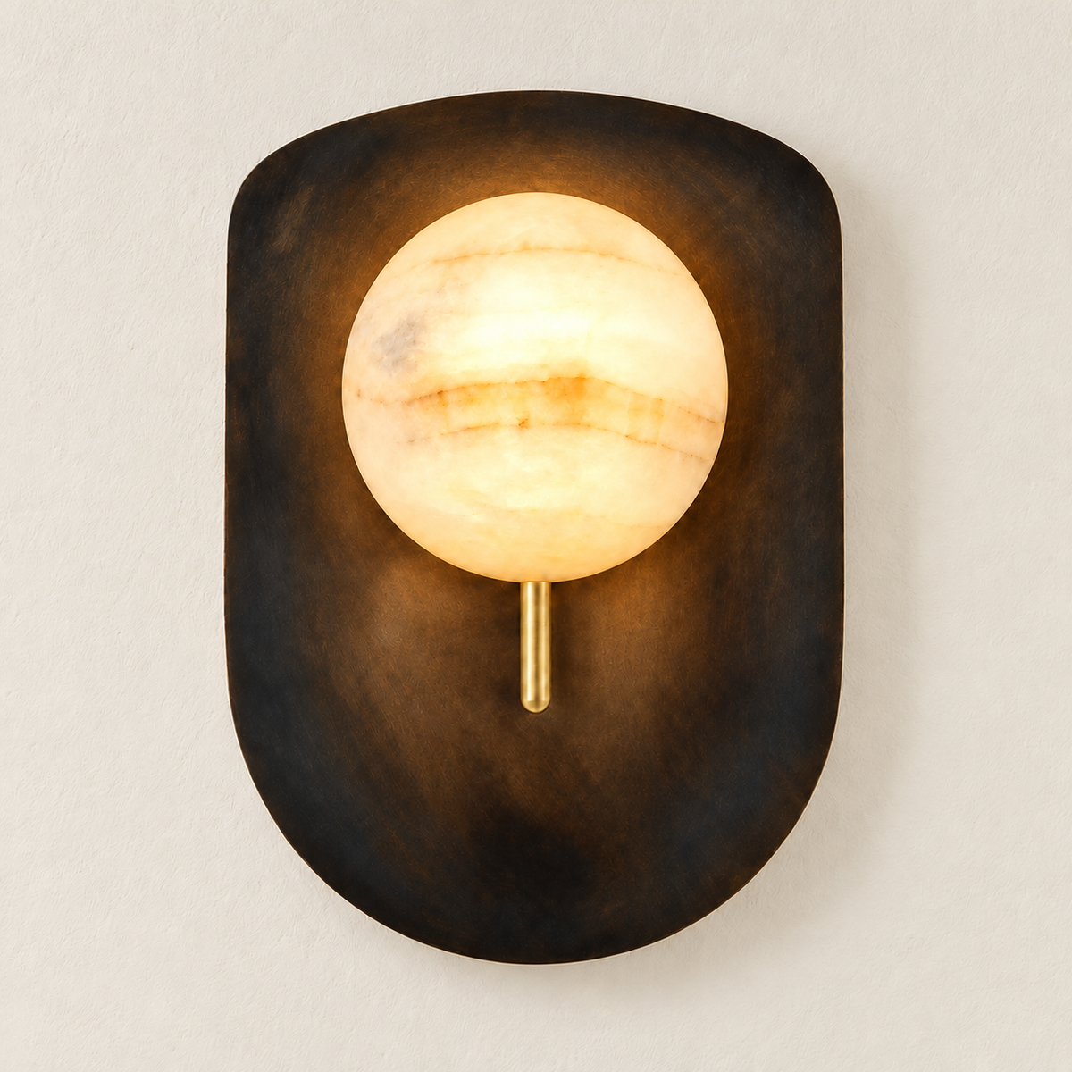 Alabaster brass shield wall sconce mounted on ivory plaster, illuminated.