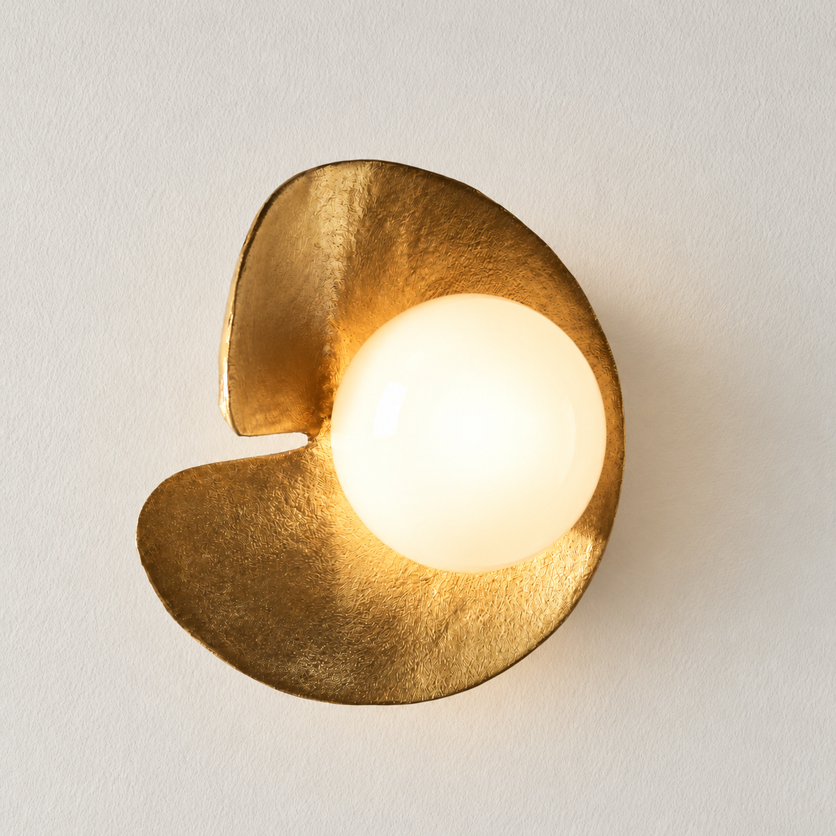 The same Aulia copper sconce with its glass globe illuminated.