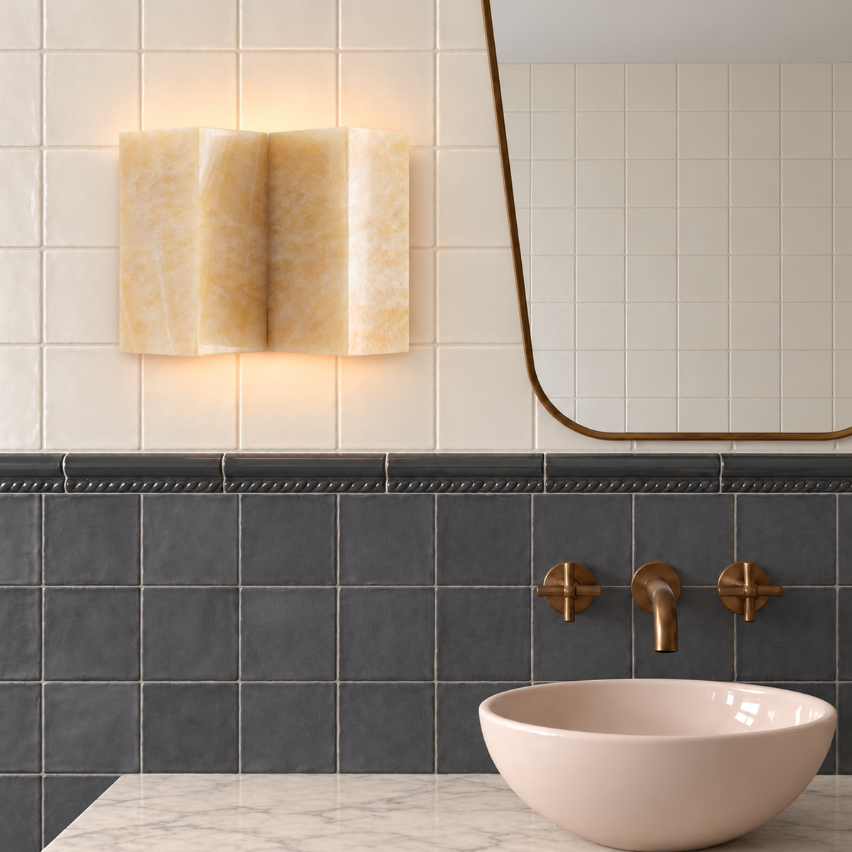 Wide jade wall sconce beside a brass mirror in an ivory and charcoal tiled bathroom.