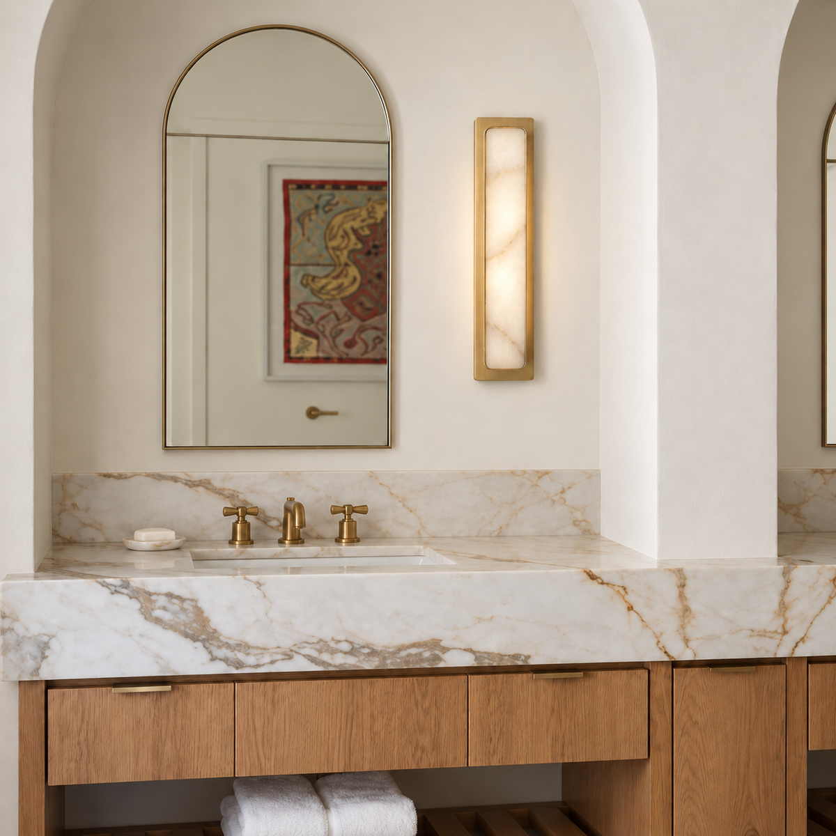Mont alabaster and brass wall light beside an arched bathroom mirror.