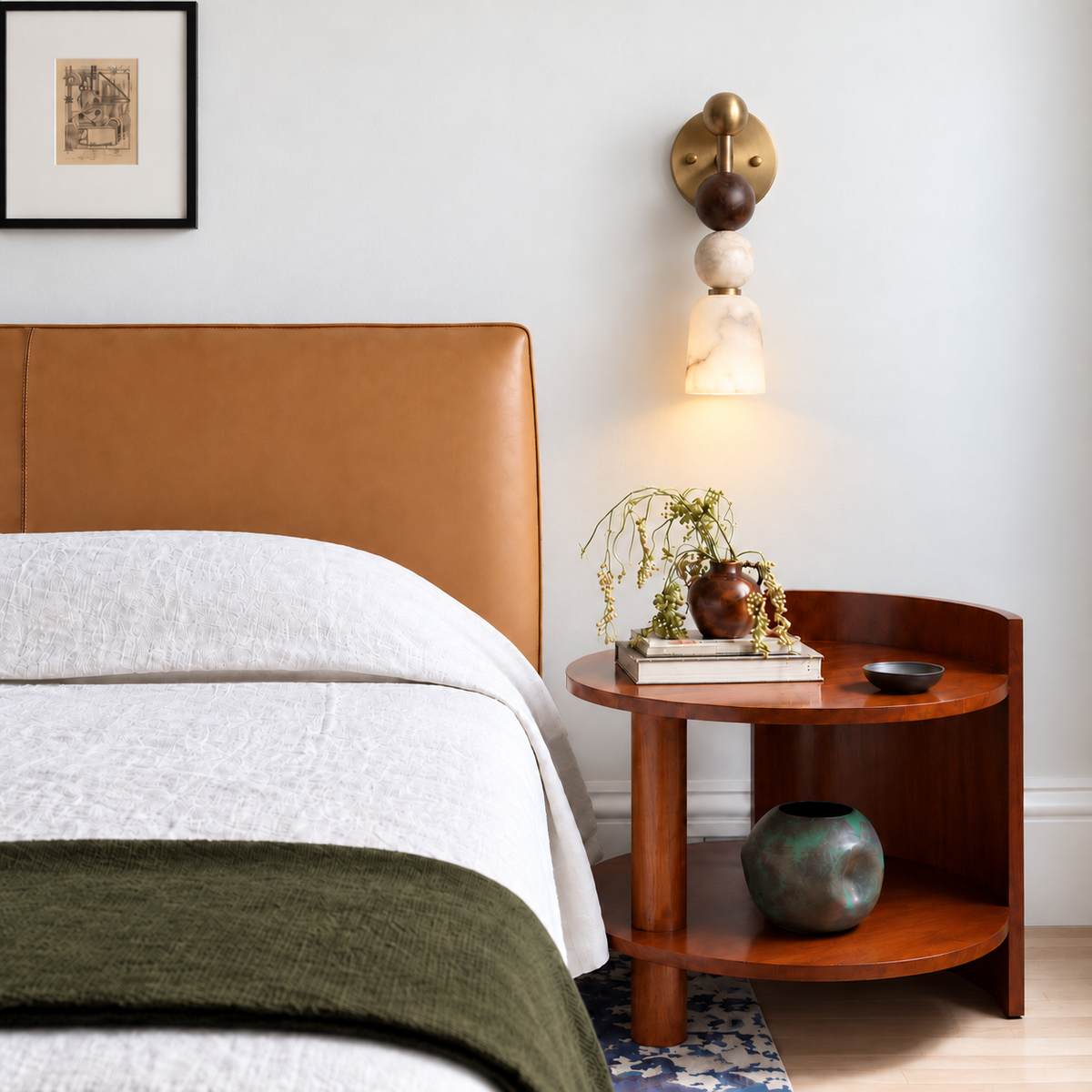 Alabaster and brass wall sconce installed above a walnut nightstand beside an upholstered bed.