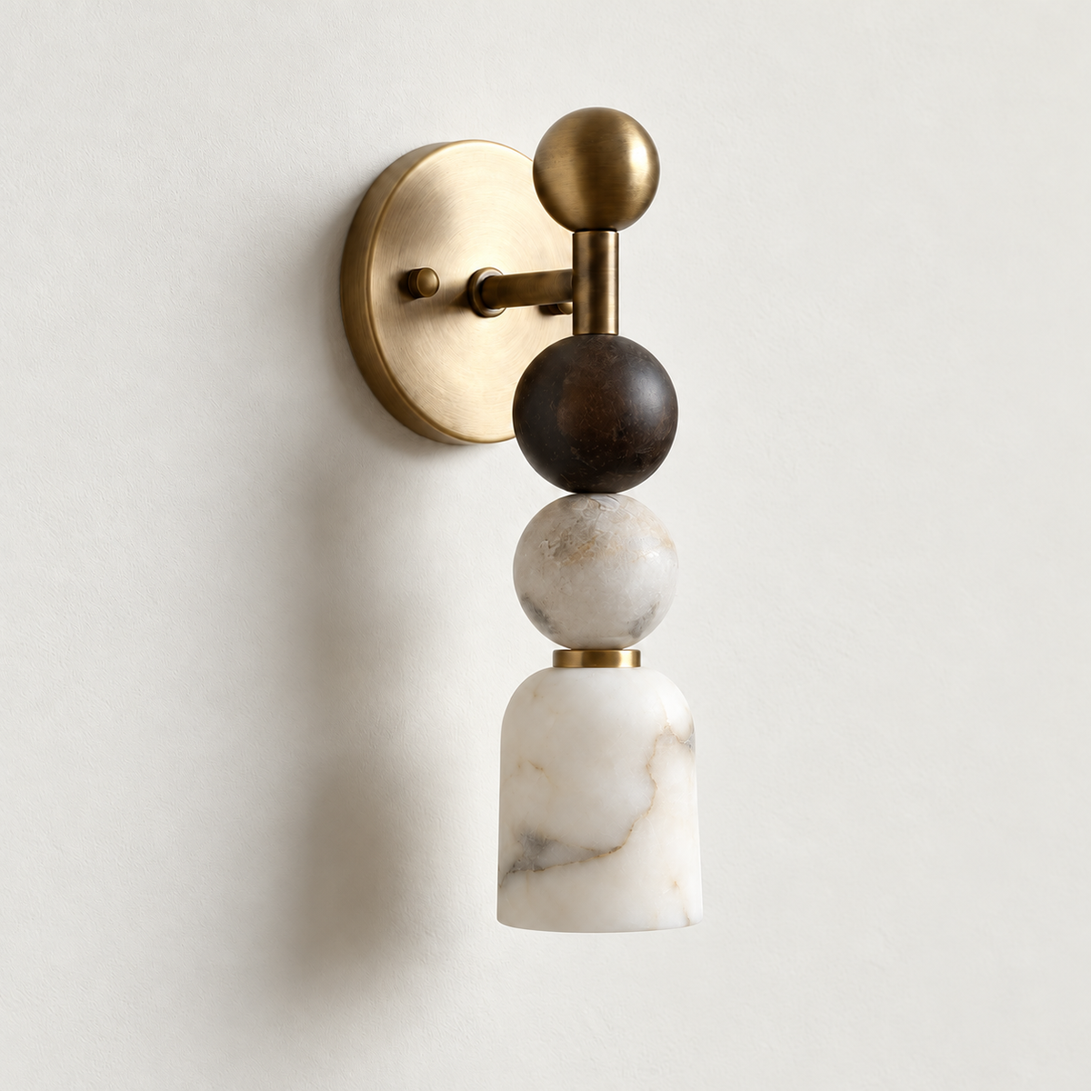 Unlit alabaster and brass wall sconce with stacked spherical details, viewed at an angle on warm ivory.