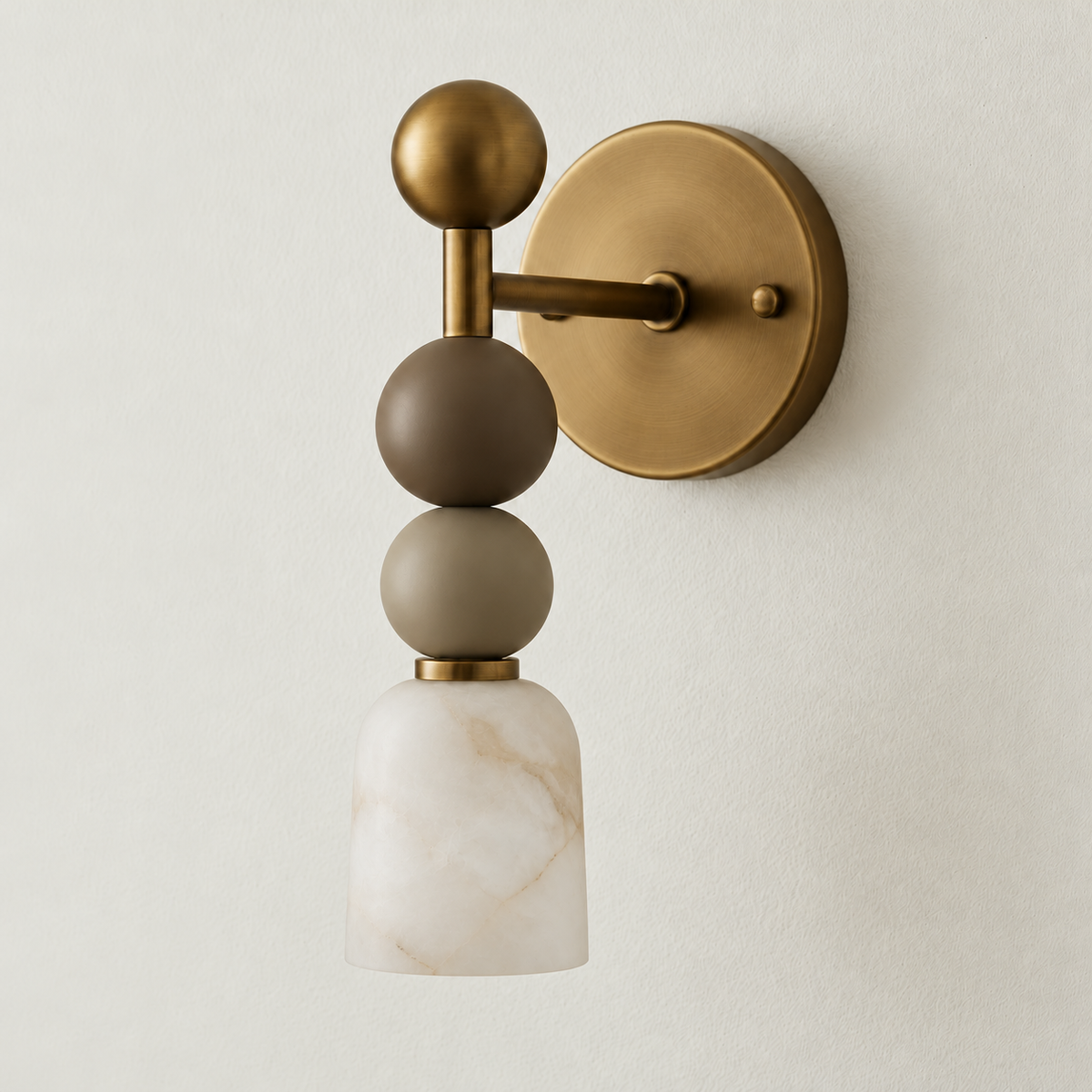 Alabaster and brass wall sconce with stacked spheres unlit on warm ivory plaster.