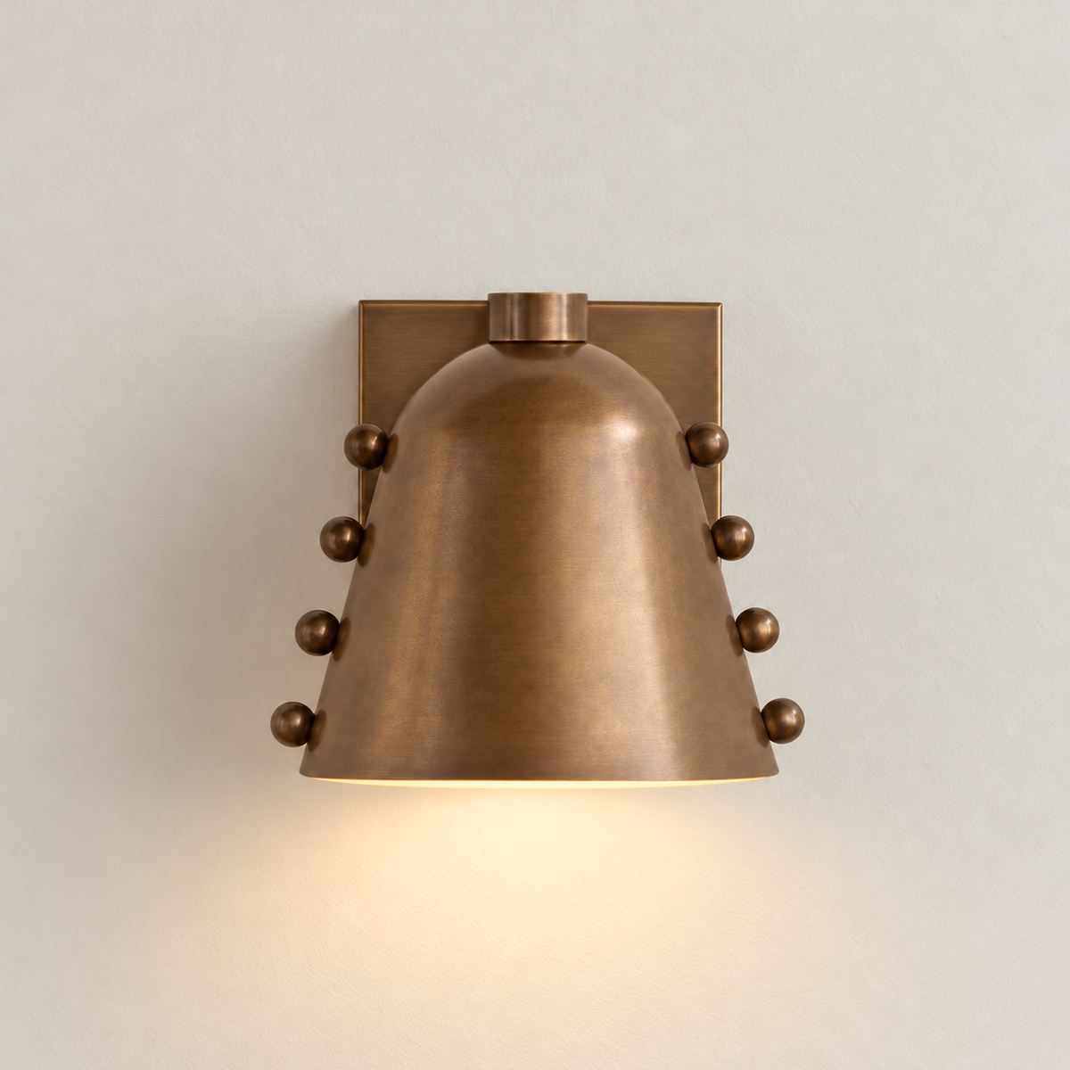 Antique brass cone wall sconce casting light downward.