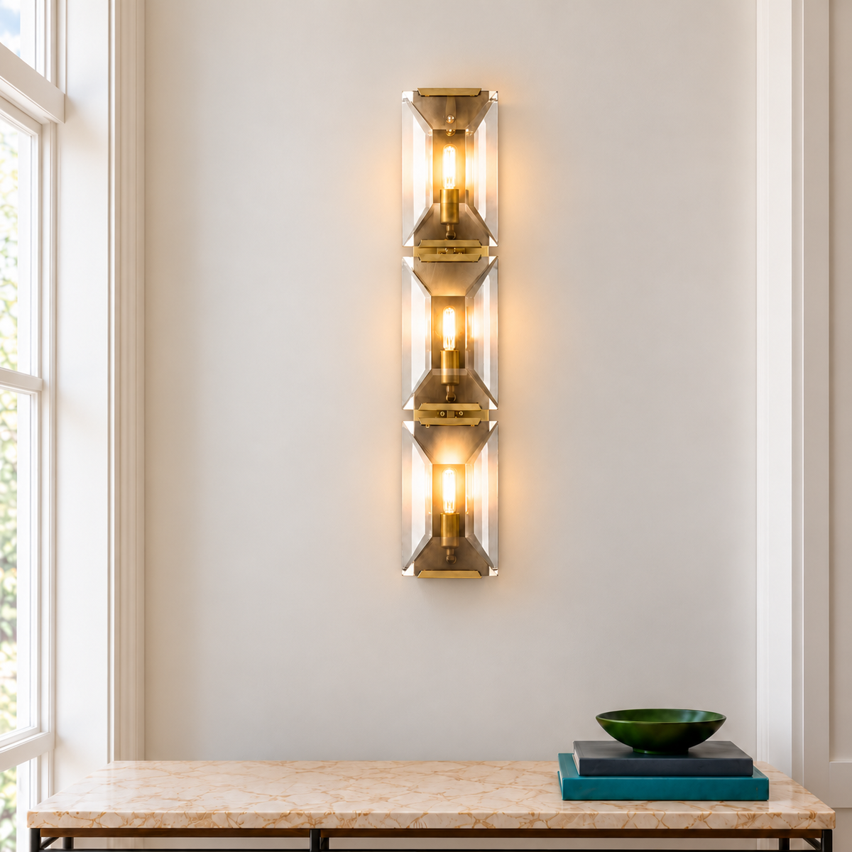 Triple crystal and brass wall sconce above a marble console beside a tall window.
