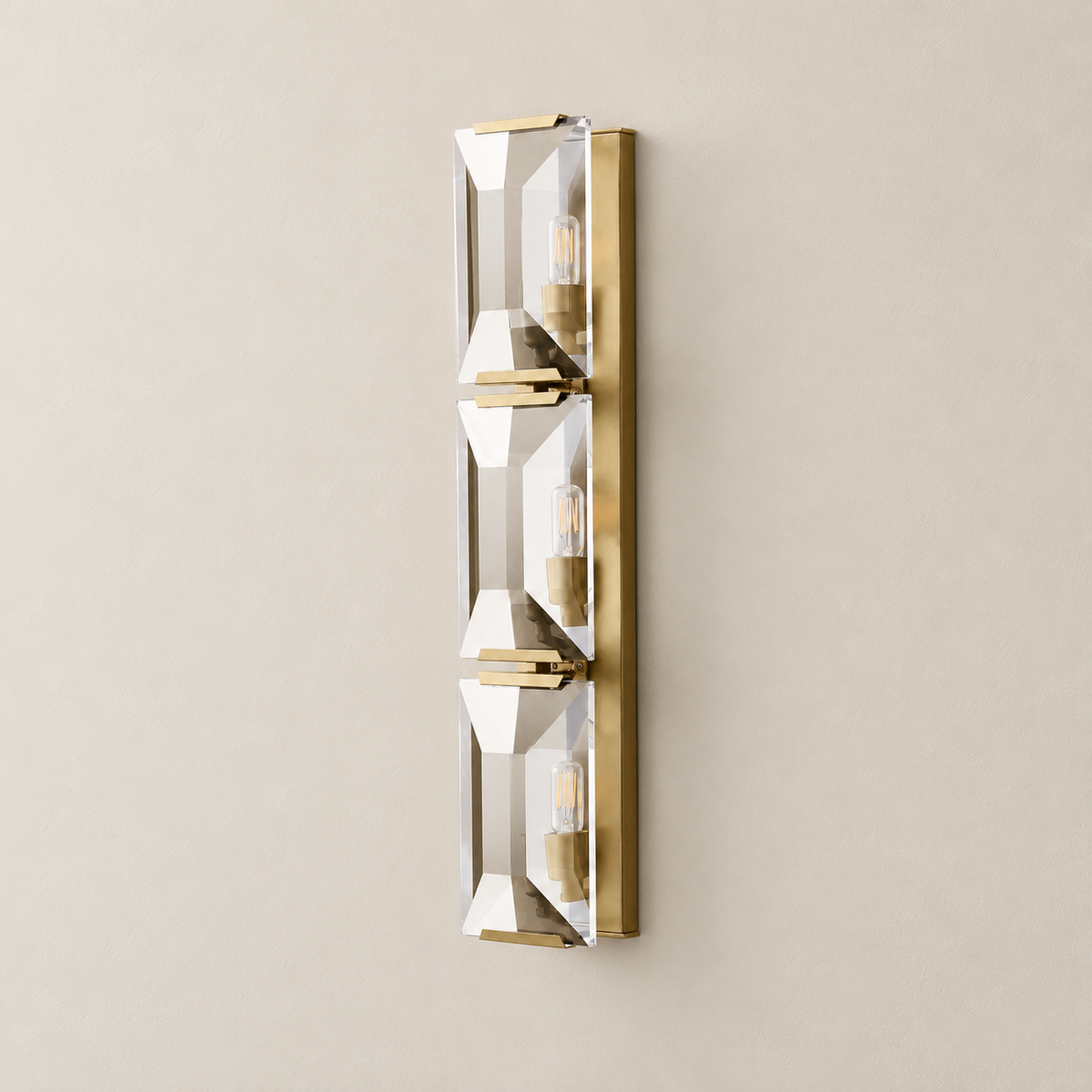 Angled view showing the triple crystal sconce’s long brass backplate and panel brackets.