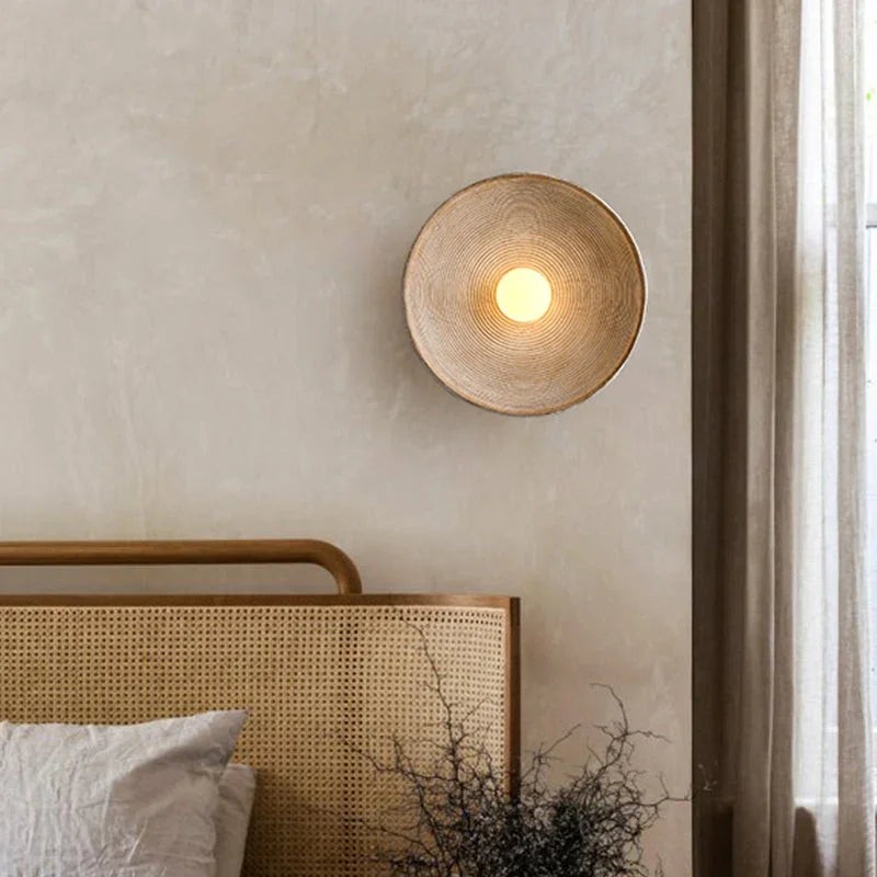 Round wabi-sabi iron wall light glowing warm in a hallway